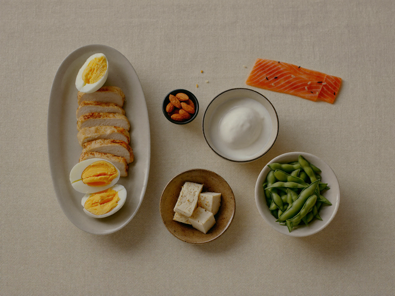 High-protein whole foods — eggs, salmon, chicken, tofu and edamame on a linen surface